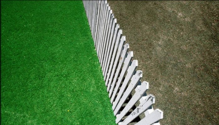 White picket fence dividing lush green lawn from dry brown grass